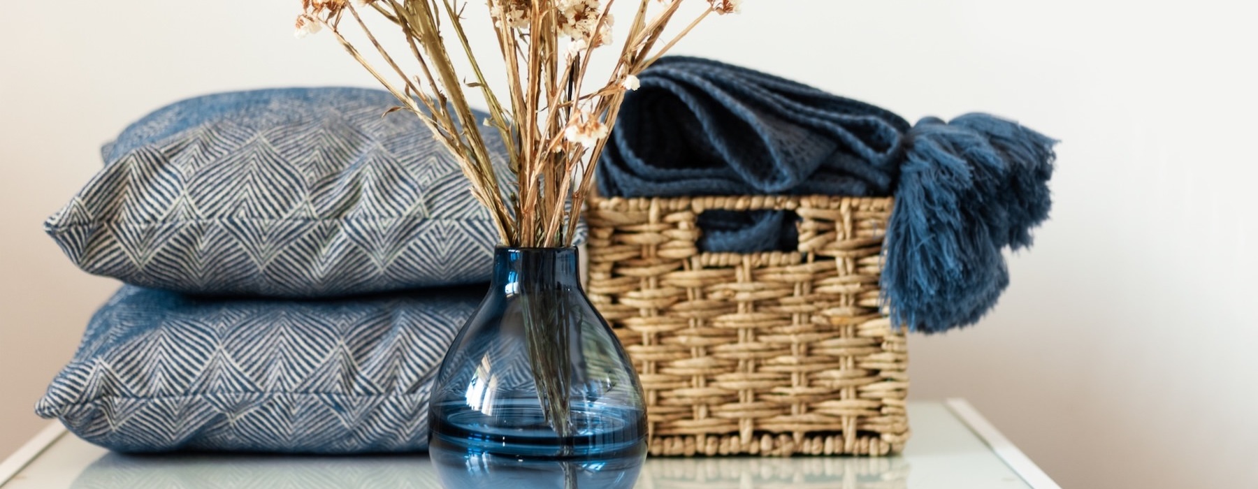 a vase with flowers, pillows and a blanket in a basket